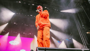J Balvin oli silminnähden otettu saamastaan vastaanotosta. Oranssiin asuun ja punaisiin aurinkolaiseihin pukeutunut kolumbialaisartisti J Balvin hymyilee Ruisrockin Niittylavalla.
