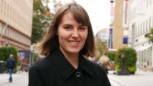 Emma Strömberg i Åbo. Emma Strömberg ler i kameran, fotad på gågatan i Åbo Svart kappa och pagehår