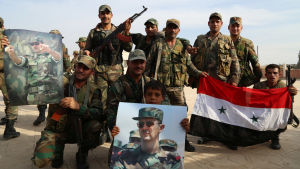 Syriska regeringsstyrkor poserar för en bild. Som rekvisita har de Syriens flagga och bilder på Bashar al Assad. 