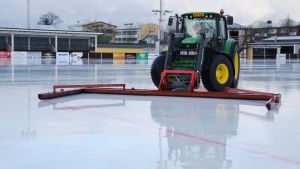 En traktor med långa gummiskrapor föser bort vatten från bandyplanens yta. Traktor "sopar" bort vatten från centralidrottsplanen i Borgå 17.02.20