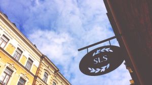 Svenska Litteratursällskapets frågeformulär kan fyllas i åtminstone fram till slutet av juni. SLS metallskylt på Riddaregatan i Helsingfors fotograferad underifrån mot en blå himmel.