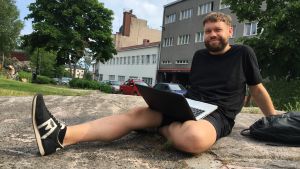 Äänisuunnittelija Niklas Nybom kuuntelee edelleen podcasteja nukkumaan mennessään. Niklas Nybom istuu hymyillen työhuoneensa ulkopuolella puistossa läppärin kanssa