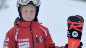 Ivar Nylund drömmer om en karriär som proffsskidåkare. En pojke med röd skiddräckt, hjälm och skidglasögon står med ett par skidor i hand