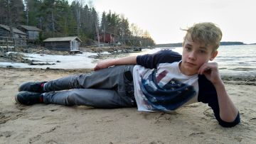 Oliver ligger på en strand och ser in i kameran.