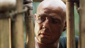 Nej, Kurtz (Marlon Brando) är inte den enda som är galen. Walter E. Kurtz (Marlon Brando) står vid ett bambustängsel och ser fundersam ut.