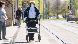 Delstaterna går sina egna vägar och för tillfället är Tyskland ett enda stort lapptäcke av olika regler för att förhindra spridningen av viruset. En gatubild med tre kvinnor som alla bar munskydd. En kvinna ses från sidan där hon står och väntar på spårvagnen. Bredvid henne går en kvinna med en rollator med ansiktet mot kameran. I bakgrunden en tredje kvinna på väg mot hållplatsen.
