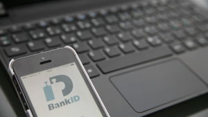 Man ska aldrig lämna ut sina lösenord och bankkoder på nätet. Smarttelefon med bank-id öppet framför en bärbar dator.