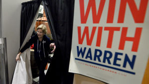 Elizabeth Warren tävlar delvis om samma väljare på vänsterkanten som Bernie Sanders. Tidigare på hösten toppade hon flera mätningar men understödet har dalat en aning i takt med att Iowavalet närmar sig. Kvinna går igenom gardiner till sitt kampanjmöte. Kvinnan är Elizabeth Warren.