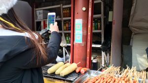 Pekingissä katuruokakin maksetaan mobiilisti. kiinalainen nainen maksaa mobiilisti katukeittiössä
