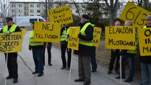 Starka känslor har präglat fusionsprocessen och sakargumenten har stått sig dåligt mot känsloargumenten, menar Tomas Häyry. Nio personer står med gula plakat med sloganer mot en kommunsammanslagning.