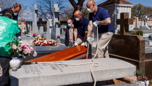 Begravning i Madrid i Spanien. Personer i skyddsmasker hissar ner en kista i en grav.