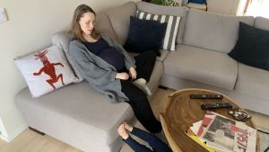 Höggravid och förkyld. Carina Bruun i Helsingfors vet att förlossningen påverkas av att det är coronaepidemi . Carina Bruun sitter höggravid på soffan och hennes två-åring ligger på golvet.
