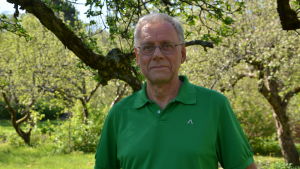 Mikko Hupa är professor och tidigare rektor vid Åbo Akademi och brukar ofta tala om Gadolin för utländska gäster som kommer till universitetet. Mikko Hupa, en man med glasögon och grön skjorta, står bland äppelträd.