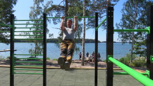Joakim Mäkelä testar det nya utegymmet Furusport i Bromarv. En man jumppar, drar armhävningar på ett utegym. Sommar, sol, hav i bakgrunden.