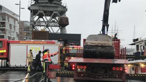 Lyftoperationen tog ett par timmar och bland annat räddningsverkets dykare deltog. Räddningspersonal ser på en rostig Saab 900 som lyfts upp ur Aura å.