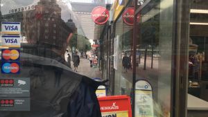 Ungefär tre procent av finländarna uppger att de har problem med spelande. En man står utanför en R-kiosk och människor går på gatan omkring honom. Bilden är arrangerad.