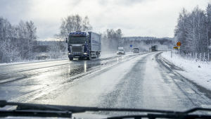 Lastbilar och personbilar på en våt landsväg på vintern.