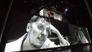 Eero Ritala som de tre systrarnas bror Andrej. Högst uppe på scenen Anna-Maija Tuokko som hans hustru Natasja. Eero Ritala som Andrej i Kolme sisarta på Nationalteatern.