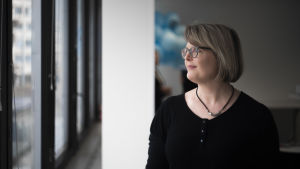 Biträdande borgmästare Sanna Vesikansa rekommenderar att man hellre ringer mormor än hälsar på medan viruset sprider sig. En kvinna ser ut genom ett fönster. Bakgrunden är relativt mörk.