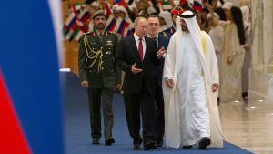 Vladimir Putin med Abu Dhabis kronprins Mohammed bin Zayed al-Nahyan spatserar på en blå matta. I bakgrunden syns Abu Dhabis flagga och till vänster i bilden syns Rysslands flagga. 