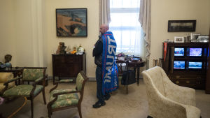 En man inne i talman Nancy Pelosis arbetsrum. Man med Trumpflagga som mantel.