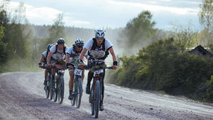 Terrängcykeln kan komma väl till pass under loppets gång. Fyra terrängcyklister på en dammig grusväg.