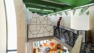Bladhuset är känt för sin fantasifulla arkitektur och färgglada insida. Här ser man bron som leder till ett av sovrummen. övrevåningen i lövhuset. en vy över träväggar, former av skog i träbrickor, svarta staket, och en vy till nedrevåningen med ett runt bord och några stolar.