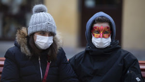 Personer som reser till Italien uppmanas vara försiktiga. Två personer i ytterkläder och munskydd står bredvid varandra och tittar åt sidan.