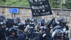 Polisens befogenheter har ökat betydligt efter att säkerhetslagen infördes. Majoriteten av Hongkongborna anser att polisen redan har använt olagligt hårdhänta metoder för att kväsa protester. Poliser i svarta kläder och hjälmar håller i en skylt som varnar för tårgas