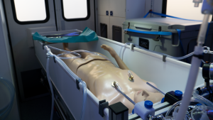 Ambulanssin sisällä nukke jääkylpyammeessa ja letkuissa.