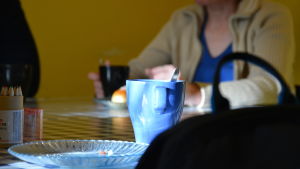 Enligt missbrukararbetaren Pertti Kenttä har många utsatta egna hemliga stödlösningar. Där de flesta ser Elokolos kafé som en plats där man äter en förmånlig bulle, ser till exempel Tassen Elokolo som en plats att hålla pengarna i förvar. En kaffemugg och smulor på ett fat. I bakgrunden sitter en person och njuter av kaffe och bulla.