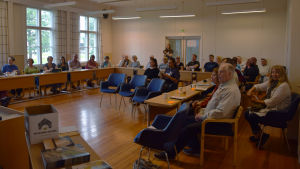 Många var på plats vid presentationen på Wilhelmsdal i Ingå Personer sitter på stolar och lyssnar under ett möte.