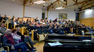 Västnylänningarna gick man ur huse för vargmötet på Lärkkulla i Karis. Människor sitter i ett auditorium. I förgrunden syns ett svart piano.