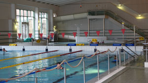 Många motionssimmar och vattenlöper i den stora bassängen. En simhall där några motionärer simmar.