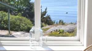 I flygelns övre våning är fönsterglasen redan på plats. Fönster med utsikt över klippor och hav i Hangö en varm sommardag. Glasburk på fönsterbrädet.