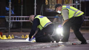 Två poliser undersöker något på marken vid några byggställningar.