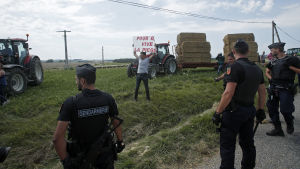 En protesterande bonde övervakas av flera poliser under den 16:e etappen i Tour de France. En protesterande bonde bevakas av flera poliser.