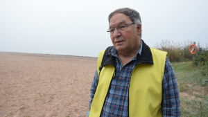 Ralf Sundberg har bott cirka fem år i Hangö och är förtjust i stadens säregna och vackra natur. en man med blårutig flanellskjorta. Ovanpå en gul reflexväst. Han står på en sandstrand.