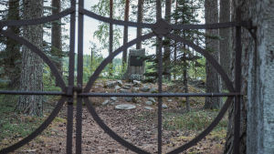Etualalla rautaportti, taustalla hautakivi metsäisellä tontilla.