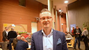 Juhani Aspara från Skanska. Man tittar in i kameran. I bakgrunden synns andra människor som diskuterar något.