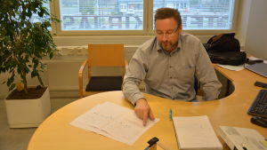 Ted Bergman med ett schema över hur processen fortskrider. Ted Bergman sitter vid sitt skrivbord med papper framför sig.
