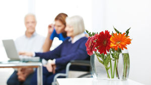 Seniorby eller seniorboende? Sjundeå är i trängande behov av nya lokaler. Antalet över 75-åringar i Sjundeå kommer att öka avsevärt på 2020-talet. Alla kan eller vill inte bo kvar i sina stora villor. några äldre och en vårdare vid en bärbar dator . Man kan inte urskilja personernas ansikten.