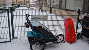 Vagnar och pulkor står parkerade utanför stängslet till daghemmet Ankdammen i Martinsbacken. I bakgrunden syns höghus.