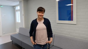 Tuula Tanskanen använder mobilapplikationen i hennes arbete. En kvinna står med händerna i fickorna och ler mot kameran.