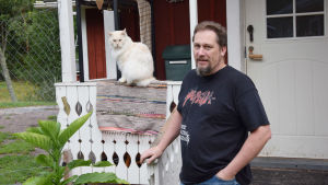 Johan Holmbergs familj i Barösund har både inne- och utekatter. En man står på en trappa i svart t-skorta. Han heter Johan Holmberg. Bredvid honom sitter en vit katt på ett staket.
