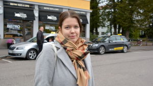 Bakom Emilia Marttinen syns taxibilarna som står vid taxistolpen utanför kulturhuset Grand. Kvinna framför Grand i Borgå.