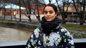 Nayab Ikram är född på Åland men bor nu i Åbo. Hennes föräldrar är från Pakistan och hon kommer satsa på en traditionell festdräkt därifrån på slottsbalen. en kvinna med pakistanskt ursprung står på en bron invid aura å i höstväder iklädd svart tjock halsduk och blommig tjock jacka.