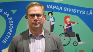 Niclas Grönholm önskar att man på riksdagsnivå skulle behandla bristen på småbarnspedagoger som inte drabbar enbart Helsingfors. Man i kostymjacka står framför mural som avbildar utbildning och fostran