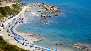 Finländarnas intresse för att resa ökar i och med coronapandemin lättat i delar av Europa. Bild av parasoll och vilstolar på en strand i Rhodos, Grekland
