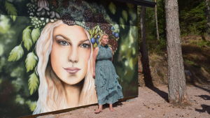 Kristina Roth på Fjärdskär. Inför starten 2018 hade mycket ändrats på ön. Det fanns nya byggnader och till och med en ny sandstrand. Allt hade gjorts utan tillstånd, uppger byggnadsinspektionen. Bilden togs när Yle Västnyland besökte ön 2018. kvinna framför konstverk på husvägg